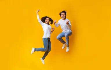 Tuinposter Cheerful girl and handsome guy jumping in air, having fun together © Prostock-studio