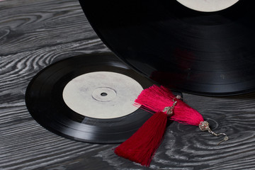 Homemade tassel earrings in red. Against the background of old vinyl records and brushed pine...