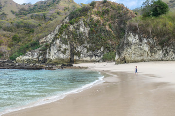 Woman walking on an idyllic Koka Beach. Hidden gem of Flores Indonesia. She is enjoying a solo escape. Waves gently washing the shore. There are hills in the back. Happiness, adventure and discovering