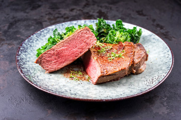 Traditional barbecue dry aged sliced wagyu sirloin beef steak with kalette and herbs as closeup on modern design plate on a rustic board
