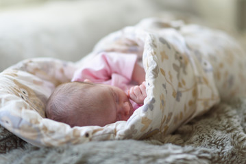 Sleeping newborn baby. Cute little girl one week old at home. Adorable lying on side covered with blanket. Shallow selective focus.