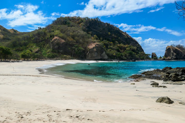 A panoramic view of idyllic Koka Beach. Hidden gem of Flores, Indonesia. Beach is gently washed by waves. Steep hills going straight into the sea. Soft clouds on the sky. Serenity and calmness