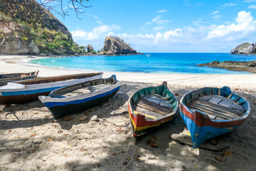 A row of colorful boats parked on a shore of idyllic Koka Beach in Flores, Indonesia. The boats are lined up under the trees, in the shade. There are some cliffs in the back. Hidden gem of Indonesia.