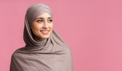 Attractive muslim woman in hijab looking away over pink background