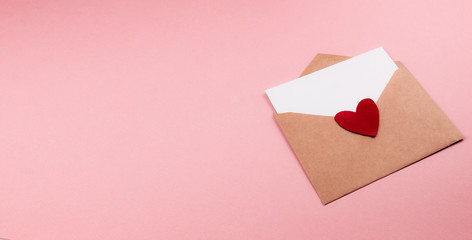 Love letter with white paper sheet in craft paper envelope with red heart flat lay on colorful pink...