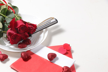Greeting card for Valentine's Day or Women's Day. Red roses with ribbon on a white plate of the gala table and a love letter with hearts, place for text. Festive background February 14. 