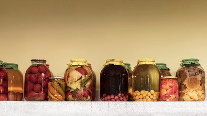 Made at home and preserved fruits, vegetables and mushrooms on a long shelf with a napkin,...