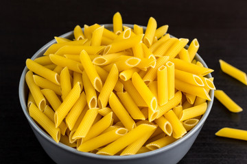black background with italian raw penne or pasta in bowl with copy space