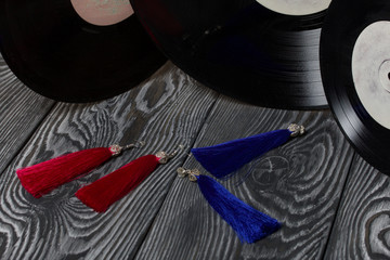 Homemade earrings tassels of red and blue. Against the background of old vinyl records and brushed...