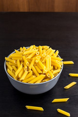 black background with italian raw penne or pasta in bowl with copy space