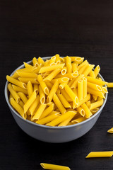 black background with italian raw penne or pasta in bowl with copy space