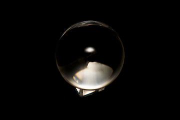A large clear crystal ball in on black background with swirling abstract designs inside on base.