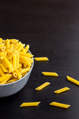 black background with italian raw penne or pasta in bowl with copy space