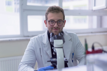 Fototapeta premium Young male scientist looking through a microscope in a laboratory doing research, microbiological analysis, medicine.