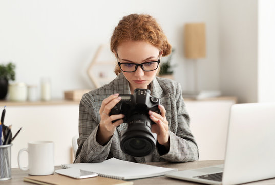 Young photographer processing images on laptop, looking at photocamera