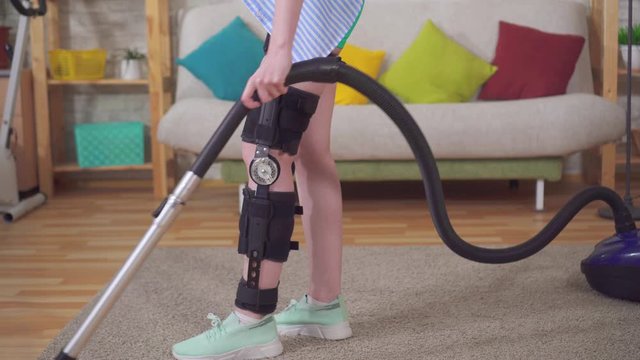 female housewife after injury knee bend orthosis knee brace vacuums in the living room