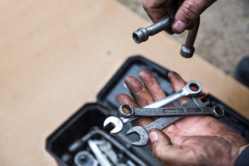 Obraz na płótnie Canvas A male mechanic is sorting out wrenches in a box with tools for repair of faulty equipment. Hands smeared with grease are holding various wrenches. Workshop and repairing