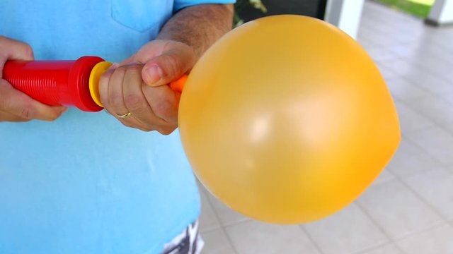 Close up of orange balloon being inflated in slow motion. Adult man blurred in backgroundd.