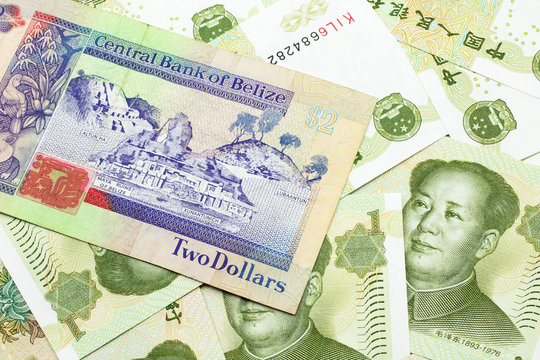 A close up image of a colorful two dollar bill from Belize with a pile of Chinese one yuan bank notes in macro