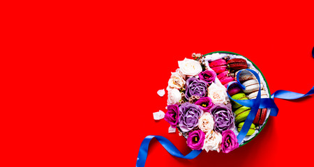 Gift box with roses in full bloom and Multicolored Macaroons. Festive blue ribbon in the shape of heart on red background. Valentines Day. Close-up