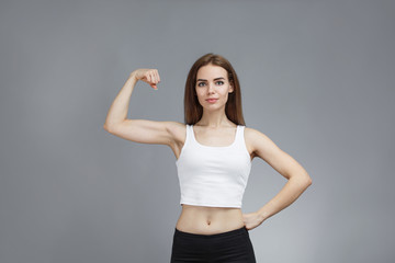 Fototapeta na wymiar woman shows her muscular arms over gray background