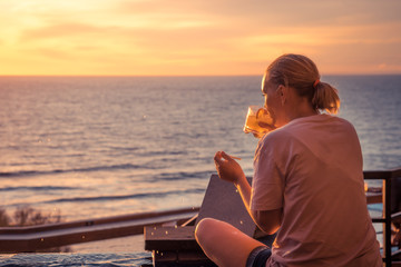 Beautiful young woman looking at horizon enjoy cocktail during travel vacation in warm colors with sunlight 