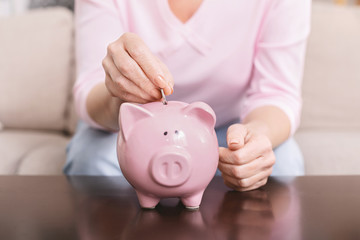 Obraz na płótnie Canvas Mature woman putting coin into piggy bank at home