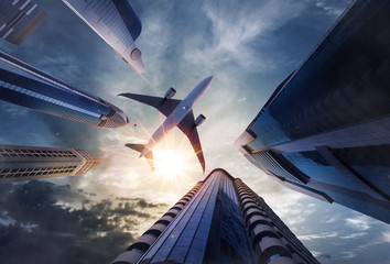 Low angle view of airplane above skyscrapers - obrazy, fototapety, plakaty