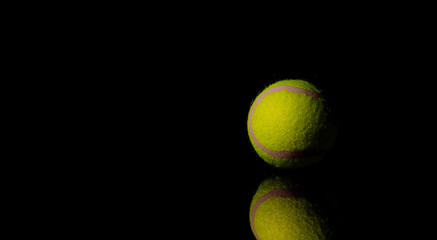 Bright Yellow Tennis Ball on dark mirror with reflections