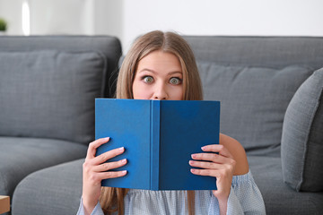 Shocked young woman reading book at home