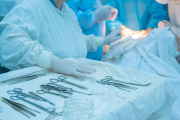 close-up, hands of a surgical nurse taking medical instruments from a sterile table, against the background of a team of doctors doing an operation