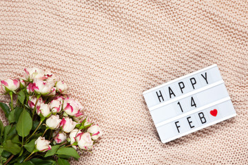 Bouquet of small roses on dusty pink blanket, lightbox with inscription Happy 14 FEB that means Valentine's Day. Flat lay. Top view. February 14th celebration concept. Horizontal, copy space