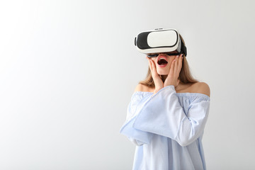 Young woman with virtual reality glasses on light background