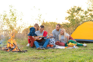 travel, tourism, hike, picnic and people concept - group of happy friends with tent and drinks playing guitar at camping