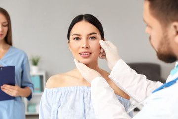 Plastic surgeon examining young woman's face prior to operation in clinic