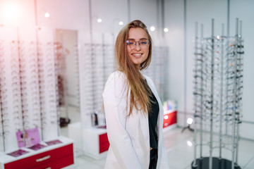 Woman in corrective glasses looking to the camera. Stand with spectacles. Wide assortment in shop.