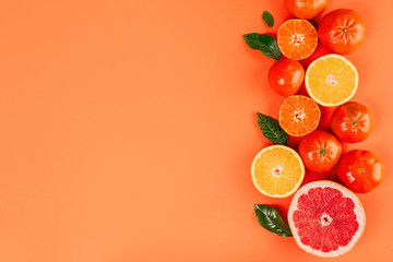 Border with fresh ripe mandarins, grapefruit and oranges with green leaves on orange background.