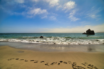 Sandy beach with ocean waves and outcropping of rocks