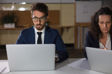 Front view of focused business people working with laptops. Concentrated managers sitting at table and using laptops. Overwork, working late concept