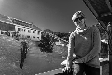 Young woman sitting on the balcony of a hotel under bright winter sun with sunglasses
