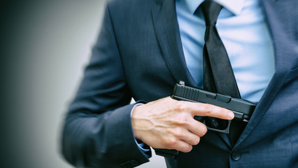 White man holding handgun in hand and covering it with his suit