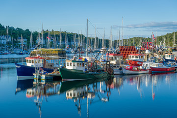 Beautiful calm day in Tarbert harbor. Colorful loal's boats and water reflections. Inner Hebrides, Scotland.