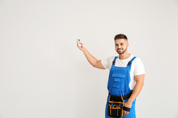 Male technician with air conditioner remote control on light background