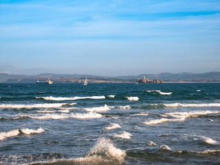 Obraz premium An oil tanker and a sailboat sail along the Cantabrian Sea near the bay of Santander with the lighthouse and the Cantabrian coast in the background