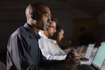 Side view of call center operator communicating with client. African American young man in...