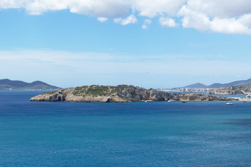Rocky sea coast with clean blue water, cloudy sky and city view. Ibiza island, Spain