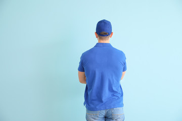 Handsome delivery man on color background, back view