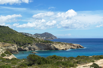 Fototapeta premium Rocky sea coast with clean blue water, cloudy sky and city view. Ibiza island, Spain
