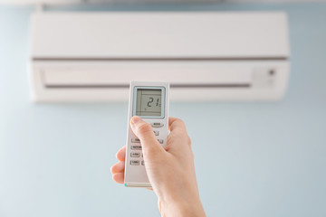 Young woman switching on air conditioner at home