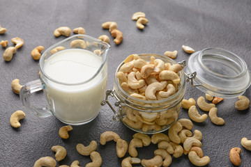 Jug of cashew milk and nuts on dark background